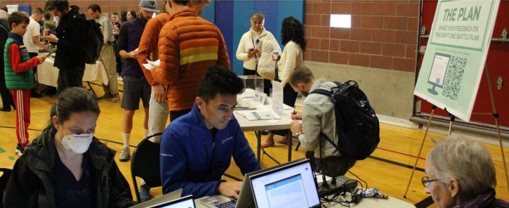 Photo of people working and gathering in a community space near a signboard titled "THE PLAN"