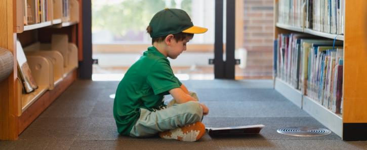 a kid sitting with abook between two bookshelves
