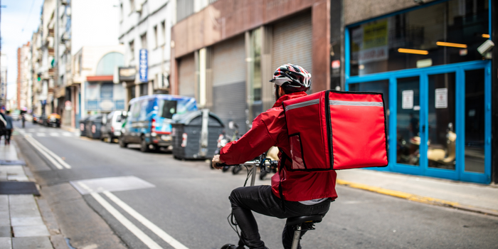 Person riding a bike wearing a helmet and cooler backpack riding through a city street