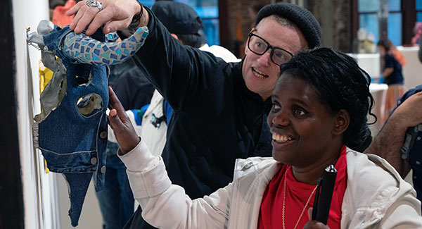 A Black blind woman and sighted guide touch a tactile artwork