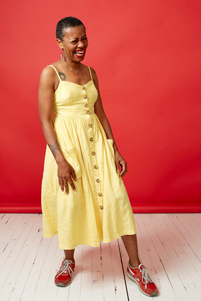 Anastacia-Ren&eacute;e smiling in a yellow dress and red shoes, standing in front of a red wall.
