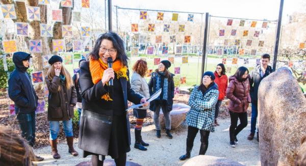 A Japanese woman stands in the Seattle Center Poetry Garden speaking into a mic to a crowd of boot campers.
