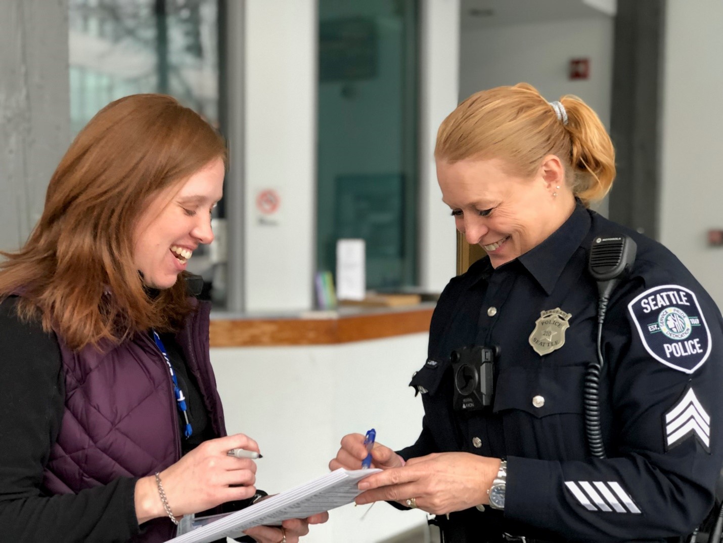 Smiling, female Victim Support Team member goes over notes with a smiling female Seattle Police officer