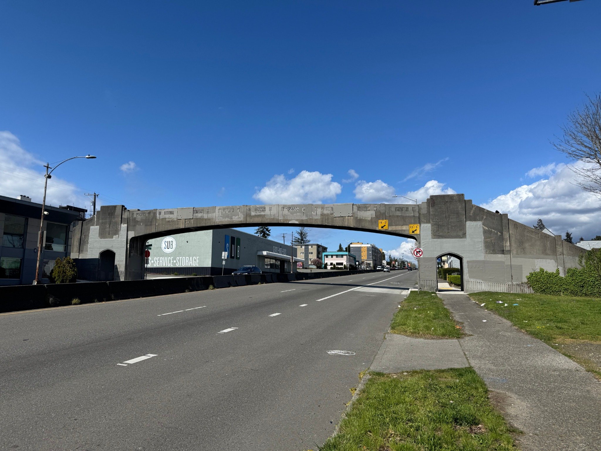 A pedestrian bridge over Aurora Ave N near N 41st St on a sunny day. Aurora Ave N and nearby businesses are also shown.
