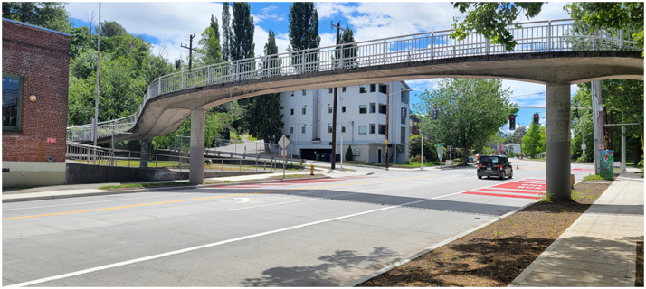 A pedestrian bridge crossing over Delridge Way SW with a ramp on the left and buildings and trees in the background.