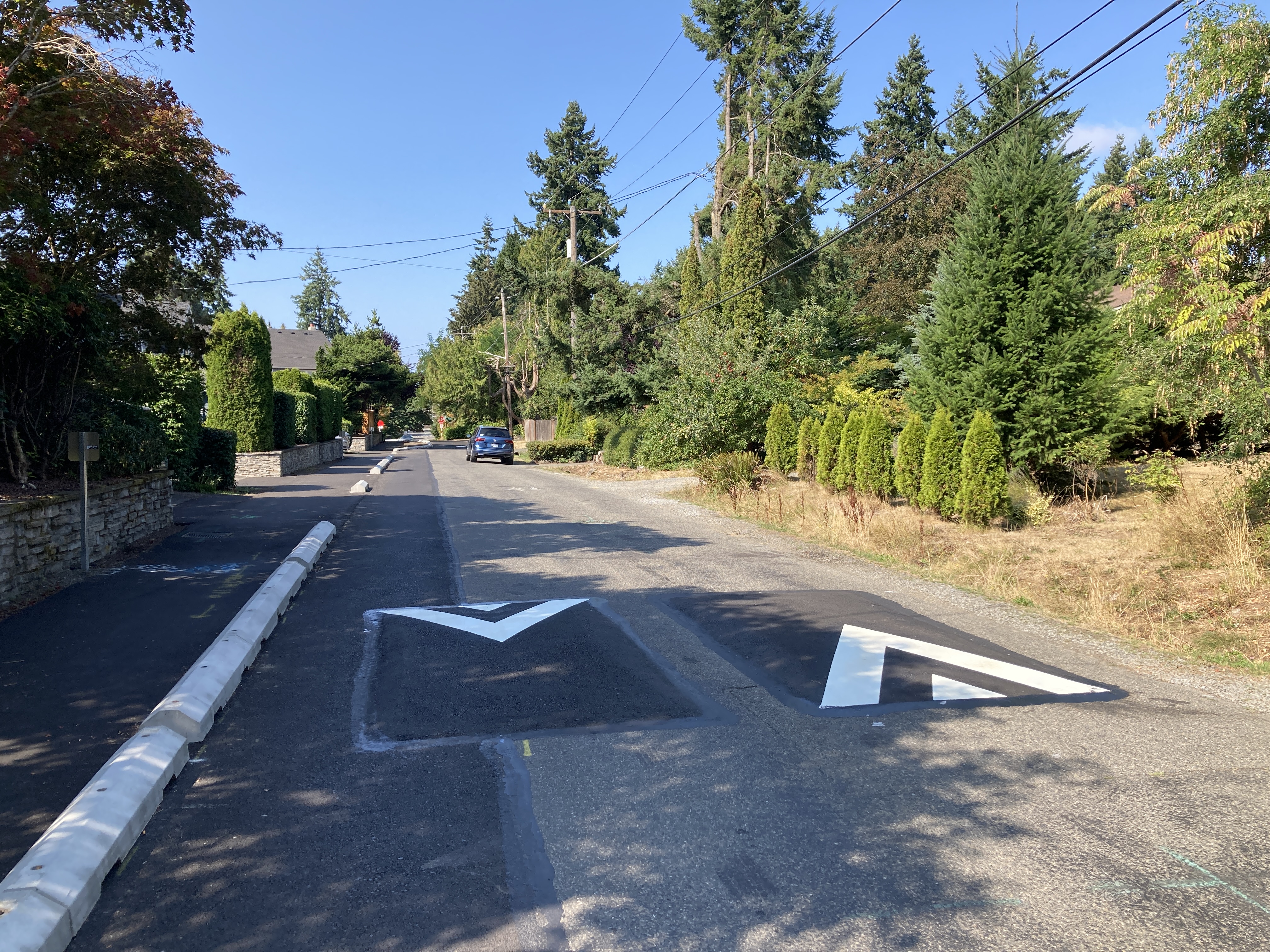 Speed cushions in traffic lane next to asphalt walkway protected by wheel stops.