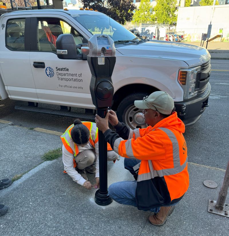 Two SDOT crew members install an IPS meter on the sidewalk in north downtown Seattle