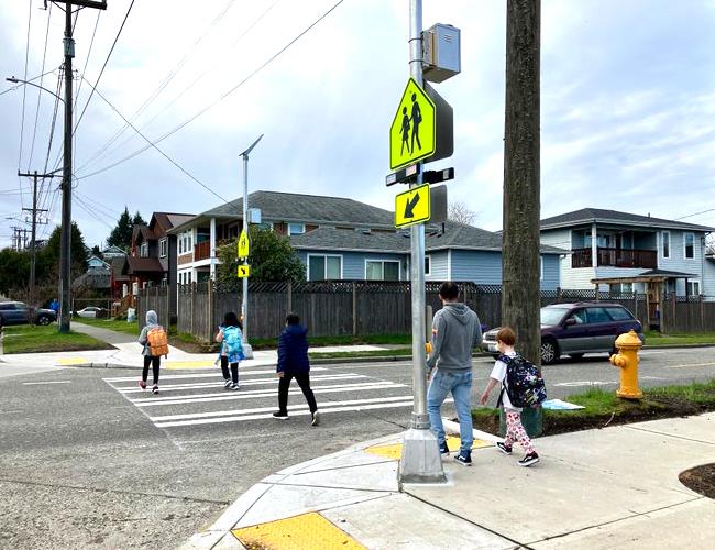 Children and an adult walking on a crosswalk with flashing crosswalk signage
