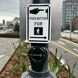 An APS signal, with lights surrounding the button and a sign that says "Push button for walk sign"" 