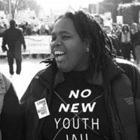 KL is turned to the side and smiling and wearing a shirt that says "no new youth jail"