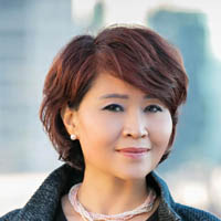 LeVihn has short, reddish-black hair, and is wearing a a necklace, earrings, and tweed jacket