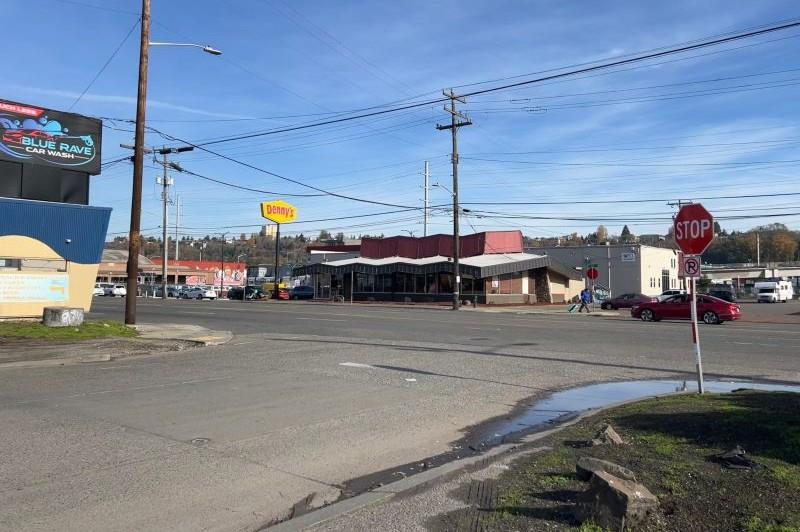 Person walks south along 4th Avenue South, crossing South Forest Street near Denny's Restaurant while cars drive along 4th Avenue South on a sunny day.