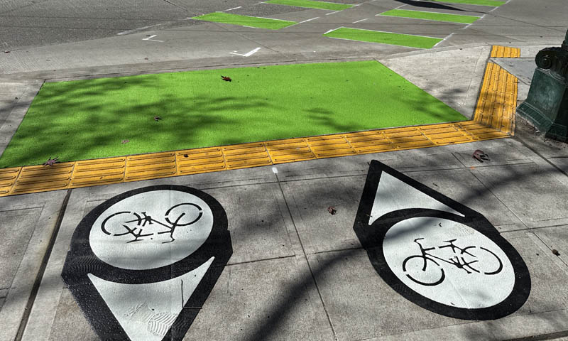 The green panel on the bike lane that rosses the intersection is wider, with two directional arrows to help cyclists know their position. There are also intermittent green stripes across the street. 