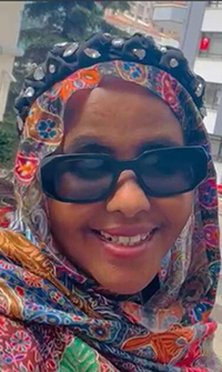 A smiling woman in a colorful head scarf and black sunglasses.