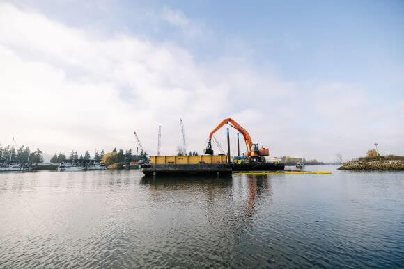 A sunny day with kayaks beached on the banks of the Duwamish with commercial vessels in background.
