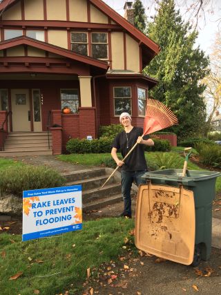 Queen Anne Customer with a rake your leaves sign and a rake in hand.