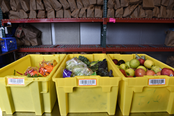 Three yellow plastic food bins full of fruits and vegetables on a shelf in a food bank.