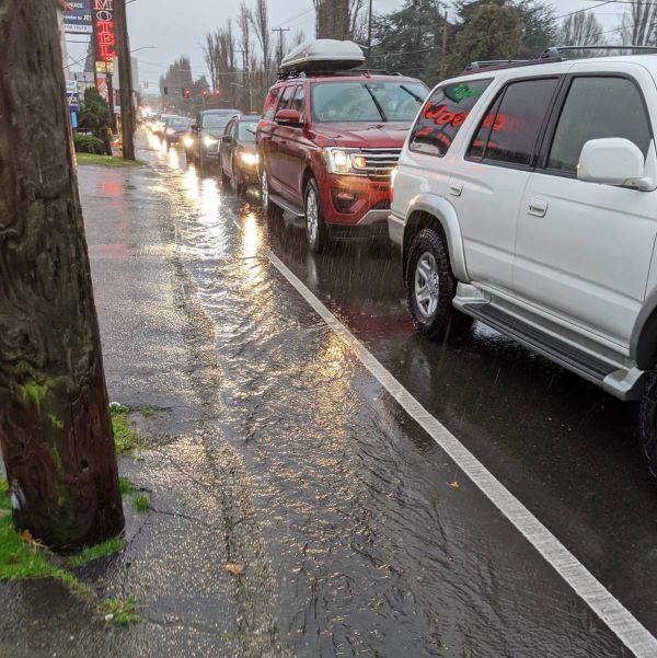 Traffic lined up on Aurora in heavy rain with overflowing gutters at the side of the road.