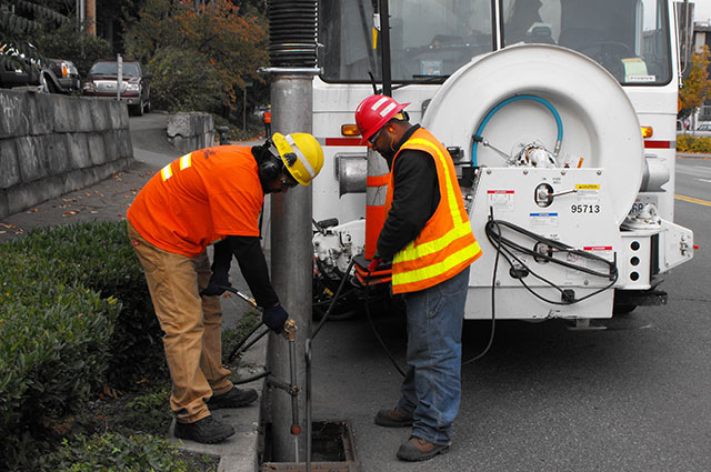 Two workers cleaning a drain with Vactor truck.