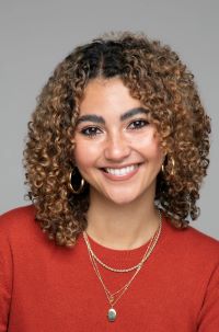 Portrait of Julia smiling broadly at the camera in a red sweater in front of a grey background 