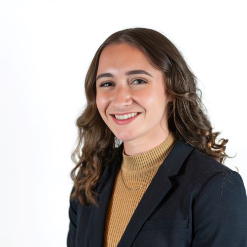 Portrait of Margaret smiling broadly at the camera in a dark blazer in front of a white background.