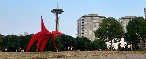 A prominent large red metal sculpture called 'The Eagle' with the Space Needle behind it. 