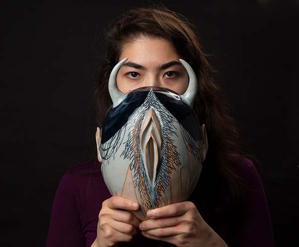 Hanako O’Leary in front of a black background holding her "War Mask 1" in front of her face,