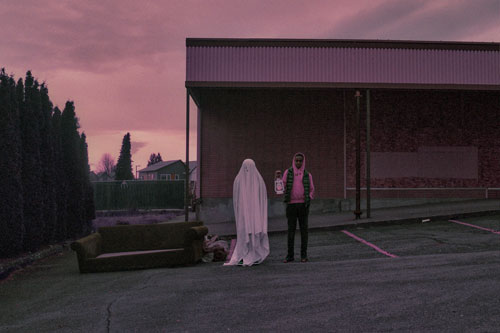 A person wearing a sheet like a ghost stands next to a young man holding a white lantern.