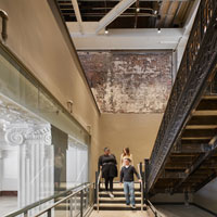 A mixture of exposed brickwork and steel beams, terrazo flooring frame a black steel staircase.