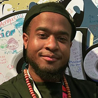 Aalijah wears a backwards cap and a necklace with large beads.