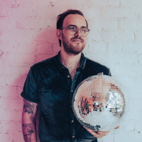 Zach wears glasses and holds a disco ball.