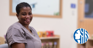 Smiling Black woman childcare worker with short black natural hair, vitiligo, and gray uniform.