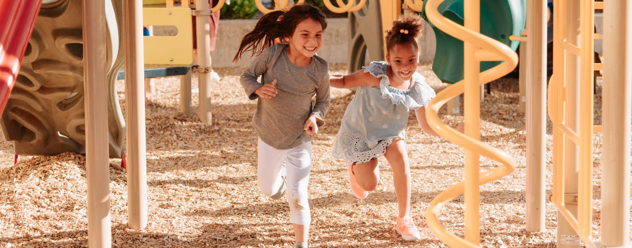 Two laughing young children running under playground equipment. (Image credit: El Centro de la Raza.)