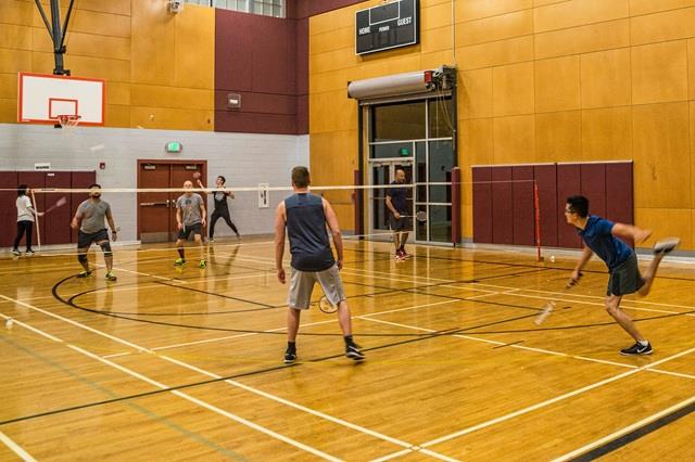 Two teams play badminton across a net in an indoor gym