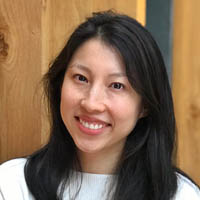 Photo of Ching Chan, smiling and leaning against a wooden wall