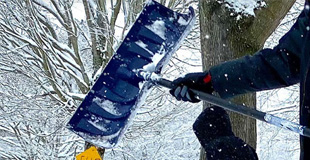 An arm holding a snow shovel and pushing out snow