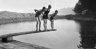 black and white photo of three people on a diving board over a lake