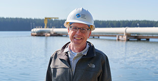 SPU employee in hardhat standing in front of Chester Morse Lake.