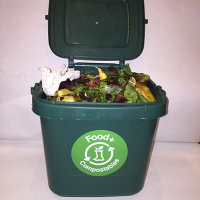 A counter top size green compost bin filled with food scraps and food-soiled paper.