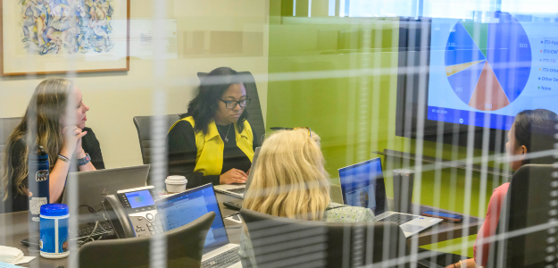 Four women working on a project with a pie chart