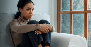 Young woman sitting by windows curled up with arms hugging knees