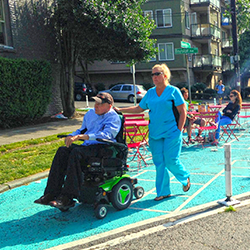 A person on a motorized wheelchair with a person walking behind them