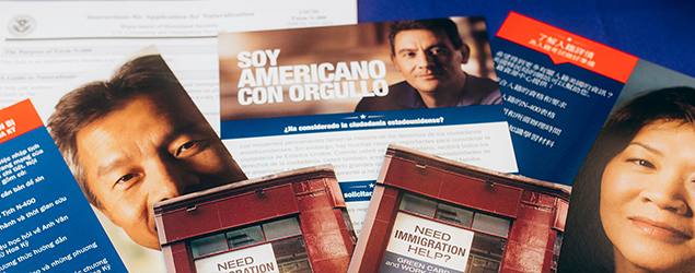 A number of colorful fliers and pamphlets in different languages about how to apply for citizenship are spread out on a table covered with a blue fabric tablecloth.
