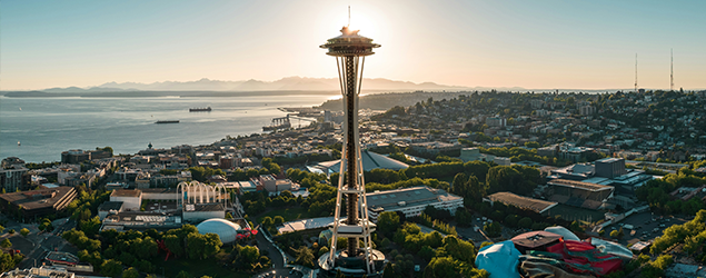 an aerial shot of seattle with the space needle perfectly lined up with a soon to be setting sun