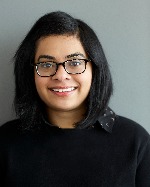 Radhika smiling broadly at the camera in a black sweater grey background